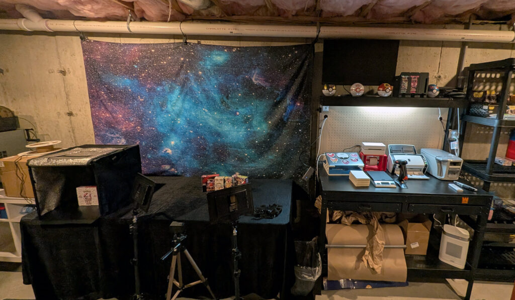 Holo Reserve basement operation wide view — photography studio on left with galaxy backdrop, shipping workbench and inventory shelving on right